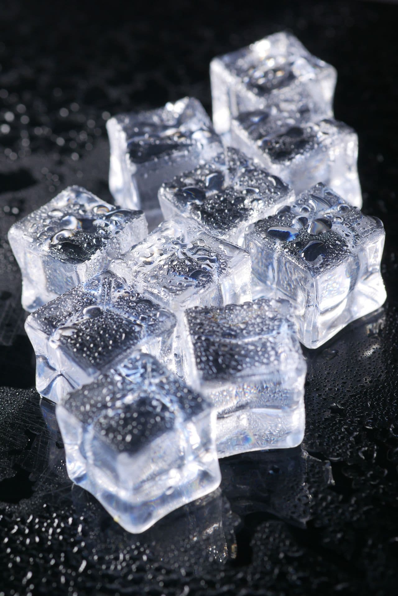 clear ice cubes from a countertop ice maker with condensation on a dark kitchen surface